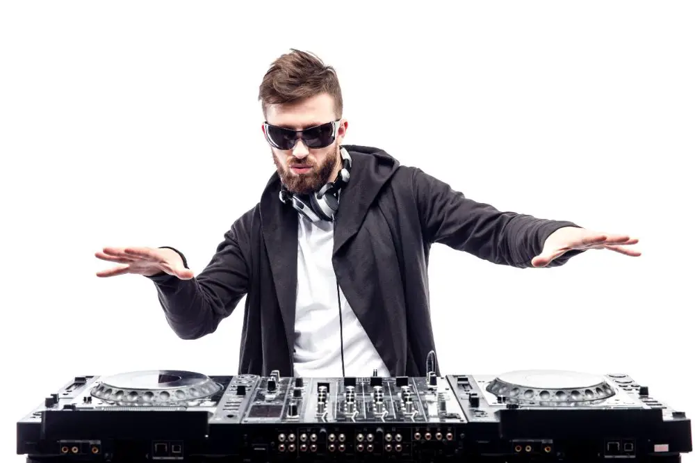 Young stylish man in black sunglasses posing with hands up behind mixing console 